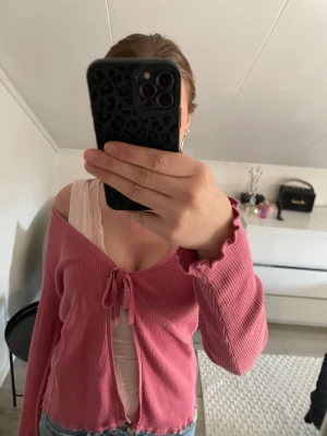 Rosa ribbad kofta från Turnover - Sitter som m/s. Söt rosa ribbad kofta från Turnover med knytning framtill och vågiga kanter. Lätt och stretchigt material, perfekt att slänga över ett linne. Långärmad och croppad modell som ger en trendig look.