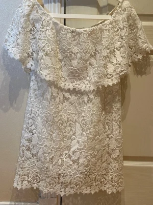 Vit spetsklänning offshoulder - Superfin vit kortklänning i spets med offshoulder-modell och vackert blommigt mönster. Klänningen har en romantisk känsla och är perfekt för sommarens alla tillfällen. Materialet är spets med fina detaljer och volang upptill.