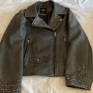Svart/grå jacka med nitar från Zara - Cool svart/grå jacka från Zara med silvriga nitar på krage och ärmslut. Aldrig använd❣️Jackan har dragkedja framtill, två fickor med dragkedja och en liten ficka med knapp. Snygg bikerstil som ger en edgy vibe till din outfit.💖