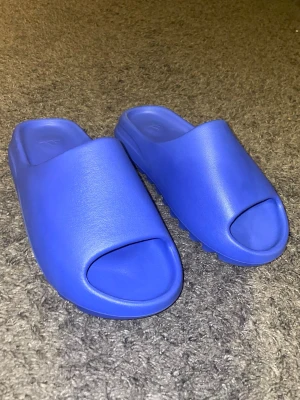 Blå Yeezy slides  - Säljer ett par blåa Yeezy slides då dem ej passar. Skick 10/10 använd ett fåtal gånger. Storlek 44,5 men är liten i storleken. Pris går att diskutera.