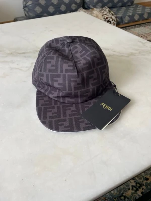 Svart keps med Fendi-logga - Snygg svart keps från Fendi med ikoniskt FF-mönster över hela kepsen. Kepsen har böjd skärm och justerbar baksida. Tillverkad i textilmaterial och har en exklusiv känsla. Perfekt accessoar för att lyfta din streetwear-stil.