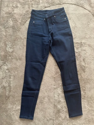 Mörkblå skinny jeans med hög midja - Snygga mörkblå skinny jeans med hög midja och klassisk femficksdesign. Jeansen har smal passform och stretchigt material som sitter tajt längs benen. Perfekta för en trendig och stilren look.