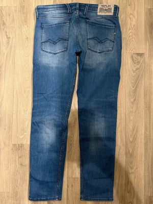 Replay Anbass Jeans Blå W34/L32 - Slim Fit - Replay Anbass blå jeans i stretchig denim med slim fit-passform som sitter både snyggt och bekvämt. Ett par riktigt mångsidiga jeans som funkar lika bra till vardag som uppklätt.  Storlek: W34/L32  * Midja: 44,5 cm * Ytterbenslängd: 104 cm * Benöppning: 17 cm  Modellen på bilderna är 185 cm lång och väger 65 kg.  Jeansen är i fint skick utan större anmärkningar. Priset är inte hugget i sten vid snabb och smidig affär!
