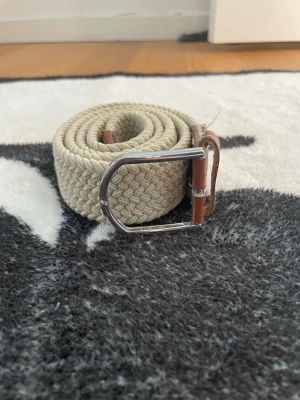 Beige flätat bälte med läderdetaljer - Snyggt beige bälte med flätad design och detaljer i brunt läder. OBS silver pinnen i mitten är borta!