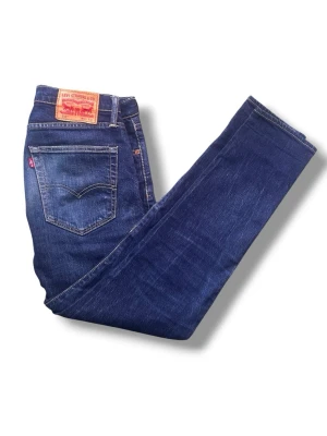 Levis jeans - Snygga mörkblå jeans med rak passform och klassisk femficksdesign. Jeansen har en knappgylf och subtila slitningar för en stilren look. Perfekta för dig som gillar en enkel och tidlös stil w30/L 32