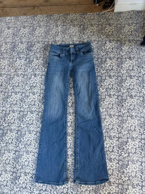 Blå bootcut jeans från Wrangler - Säljer ett par klassiska blå bootcut jeans från Nelly med snygga detaljer på bakfickorna. Jeansen är mycket low waist! 550 eller bud! 
