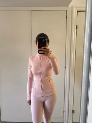 Lululemon  - Priset kan diskuteras!! Snyggt ljusrosa träningsset med figurnära jacka och matchande tights. Jackan har dragkedja framtill, hög krage och fickor med dragkedja. Setet är gjort i ett stretchigt och mjukt material som passar perfekt till gymmet eller löprundan.