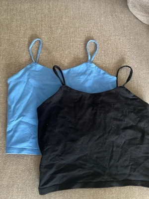 2-pack linne toppar blå & svart - Två enkla och stilrena linne toppar i blått och svart med smala axelband. Perfekta att matcha till jeans eller kjol. Tillverkade i mjukt bomullsmaterial för skön känsla. Säljes som ett paket.