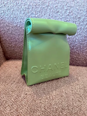 Grön smink väska necessär  - Cool liten väska i ljusgrönt, med präglad logga framtill. Väskan har en unik rullad topp och är gjord i ett slätt, glansigt material som känns modernt och trendigt. Perfekt för dig som vill sticka ut med accessoarerna.