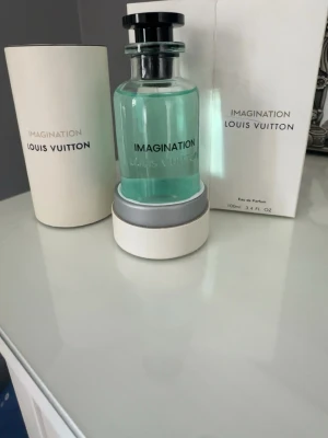 Louis Vuitton Imagination EdP 100ml - Louis Vuitton Imagination Eau de Parfum i en stilren glasflaska med turkosblått innehåll. Flaskan har svart lock och levereras i exklusiv vit förpackning. En lyxig parfym som utstrålar elegans och modernitet.