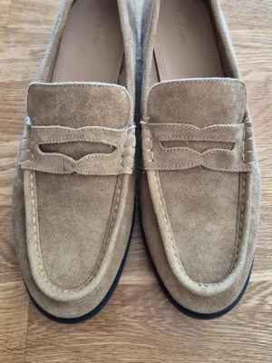 Beige mockaloafers från hm premium - H&M Premium. Beige mocka, stl 42 (27,5 cm invändigt). Aldrig använda. Nypris 890 kr.Stilrena loafers i beige mocka från hm premium med klassisk pennyloafers-design och svarta sulor. Snyggt sydda detaljer och mjukt material som ger en clean look. Perfekta för dig som gillar minimalistisk stil och vill ha något som funkar till många outfits.