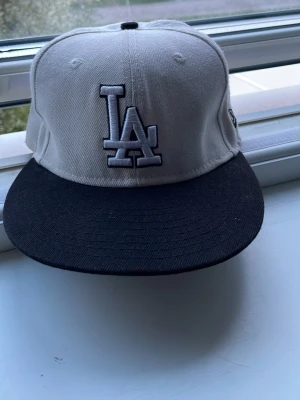 Vit LA keps - Snygg LA Dodgers keps  med vit krona och svart skärm. Broderad LA-logga framtill och Klassisk snapback-modell i bomull, perfekt för en sportig och trendig look. Storlek 55,8 cm Perfekt till sommaren☀️