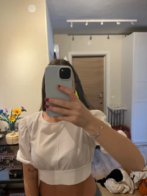 Vit croppad topp med puffärm - Säljer en vit croppad topp med puffärmar och bred resår i midjan. Toppen har en enkel, stilren look och är perfekt för dig som gillar trendiga detaljer. Materialet känns lätt och luftigt, vilket gör den skön att bära till jeans eller kjol.