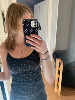 Svart prickig linnetopp - Svart linnetopp med vita små prickar. Topp med smala axelband och figurnära passform, perfekt för en trendig look. står ingen storlek men skulle säga xs/s