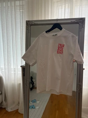 Vit Casablanca t-shirt med röd logga - Vit t-shirt från Casablanca med röd grafisk logga på bröstet och stor logga på ryggen. Klassisk passform och rund halsringning. Perfekt för dig som gillar stilrena och trendiga plagg. OVERSIZED