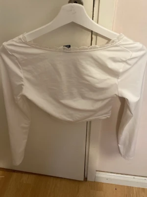 Vit långärmad topp från SHEIN - Säljer en vit långärmad topp från SHEIN i storlek XS. Toppen har en söt spetskant vid halsringningen och är tillverkad i ett mjukt, stretchigt material. Perfekt att styla med jeans eller kjol för en clean look.