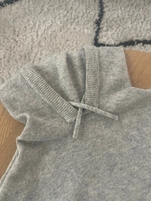 Grå Cashmere Hoodie - Hej👋 Säljer en mysig ljusgrå stickad hoodie med dragsko i kragen🙏 Tröjan har långa ärmar och ribbstickade muddar vid ärmslut och nederkant🤩 Perfekt för våriga dagar och enkel att matcha med andra plagg😮‍💨 OBS! Ett liten hål under höger arm⚠️ Meddela gärna vid frågor📩