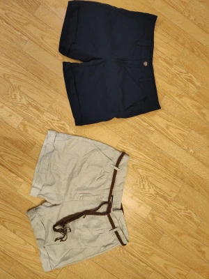 Två par shorts kortbyxor marinblått+beige dam stl 40 - Säljer två par shorts, ett par marinblå och ett par beige med brunt knytband i midjan. Båda har avslappnad passform och är perfekta för varma dagar. Mycket bra skick, endast använda 1 gång. Båda stl 40 dam.