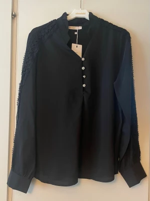 *NY*Svart finblus med spets från LaLista i stl 40, Presenttips  - Ny med prislapp. Svart tunnare blus med vackra detaljer på ärmar och krage och silverfärgade glittrande knappar. Normal i stl. 100% polyester. Längd: ca 65 cm, Byst: ca 84 cm. Nypris: 249 sek, Pris nu: 80 sek 