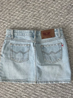 Ljusblå jeanskjol från Levi's - Snygg ljusblå jeanskjol från Levi's med slitna detaljer framtill och klassiska bakfickor. Köpt secondhand.