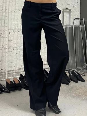 Svarta vida kostymbyxor - Snygga svarta kostymbyxor med rak och vid passform. Byxorna har hällor för skärp, två fickor fram och två bakfickor med lock. Perfekta för en stilren look och passar till många olika outfits.