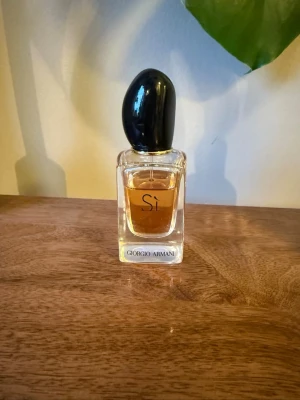 Giorgio Armani Sì Eau de Parfum - Elegant parfym från Giorgio Armani, Sì Eau de Parfum. Flaskan är genomskinlig med en svart, oval kork och innehåller en bärnstensfärgad vätska. Klassisk och stilren design som passar perfekt på parfymhyllan.