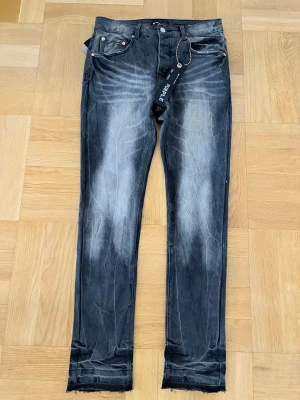 Svarta skinny jeans från Purple Brand - Säljer ett par svarta skinny jeans från Purple Brand med slitna detaljer och råa kanter vid bensluten. Jeansen har en tvättad look med ljusare partier framtill och bakfickor. Klassisk femficksmodell och knappgylf.