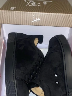 Svarta sneakers från Christian Louboutin - Snygga helsvarta sneakers från Christian Louboutin i mocka med diskreta detaljer och svarta skosnören. Låg modell med klassisk siluett och exklusiv känsla. Perfekta för dig som gillar stilrena och lyxiga skor. Skriv till mig om priset så löser vi!