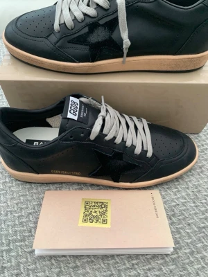 Svarta Golden Goose Ballstar sneakers - Svarta Golden Goose Ballstar sneakers i läder med beige sula och grå skosnören. Klassisk låg modell med perforerad tå och svart stjärndetalj på sidan. Märkeslogga på plösen och sidan. Snygg och stilren design som passar till många outfits.