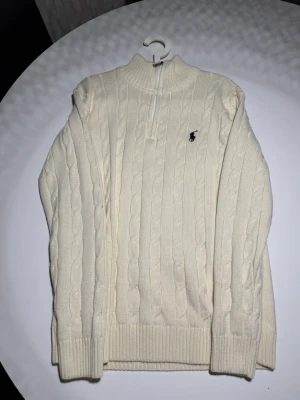 Beige zip up Ralph Lauren -  Crème/beige Ralph Lauren zip up med halv dragkedja och klassisk broderad logga på bröstet. Tröjan har ribbade muddar och hög krage, perfekt för lager-på-lager. Tillverkad i mjukt stickat material. Storlek M-L 