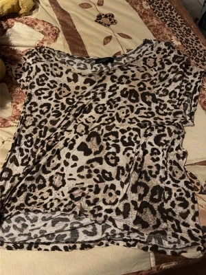 Leopardmönstrad t-shirt i bomull - Cool t-shirt med leopardmönster i beige, svart och bruna toner. Modellen är kortärmad och har en avslappnad passform. Perfekt för dig som vill sticka ut med ett djuriskt print.