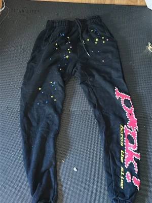 Svarta Sp5der mjukis byxor - Svarta mjukisbyxor med färgglada stjärnor och stort tryck på ena benet där det står 'prank! heres the slime' i rosa och gult. Byxorna har resår i midjan med dragsko och muddar vid bensluten. Perfekta för en avslappnad och cool stil.