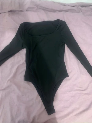Svart långärmad body med rund hals - En enkel och stilren svart body med långa ärmar och rundad halsringning. Perfekt att matcha med jeans eller kjol för en clean look. Materialet ser ut att vara mjukt och stretchigt, vilket gör den bekväm att bära hela dagen.