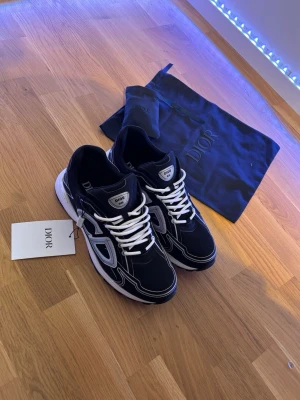 Svarta Dior sneakers med vita detaljer - Snygga svarta Dior sneakers med vita och grå reflexer. Kommer med originalpåse och tagg. De är i storlek 47 och helt nya. 