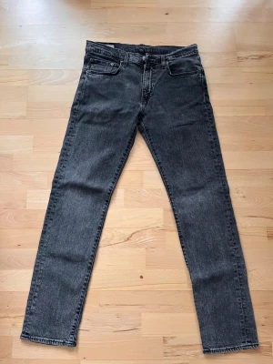 Svarta jeans från Levis - Säljer ett par svarta jeans från Levis med klassisk femficksdesign och raka ben. Jeansen har en snygg tvättad look och är tillverkade i bomull. Perfekta för dig som gillar en enkel och stilren stil. OBS har behövt sy ihop dom mellanbenen men det syns ej när dom är på!