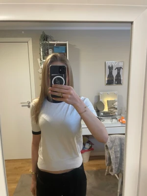 Vit topp med svarta detaljer - Vit topp med svarta muddar vid halsringning och ärmslut. Kortärmad och ribbad nedtill för en snygg passform. Enkel och stilren design som passar till det mesta.