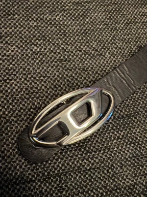 Svart diesel bälte - Bältet är snyggt men några hål har gått sönder så det är ett stort. Vet ej så mycket om skärpet men köpte det från Vinted. Längden är 105cm och bredd 3cm Hör av er vid frågor och kan gå lägre i pris!