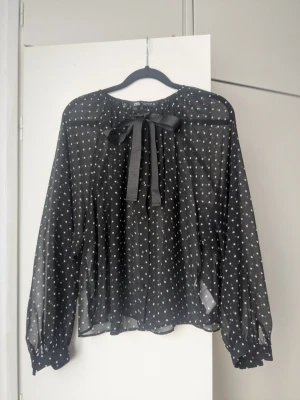 Svart prickig blus med rosett Zara - Snygg svart transparent blus från Zara med vita prickar och band som man kan knyta vid ringningen. Blusen har långa ärmar med knappar vid mudden och ett luftigt, flowy material i 100% polyesterl. Jag har bara använt den en gång så den är i perfekt skick. Kom med en vit krage jag kan skicka med i köpet som jag tog av när jag köpte den. Den är i xs/s men passar mig som är medium fint. Slutar vid höften så den passar perfekt till lågmidjade jeans/byxor 🎬