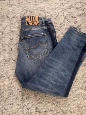 Blå jeans med djurmönstrad patch - Snygga blå jeans med tvättad look och raka ben. Bakfickorna har kontrastsömmar och i midjan sitter en unik patch med djurmönster. Jeansen har klassisk femficksdesign och är tillverkade i denim. Perfekta för en avslappnad och trendig stil.