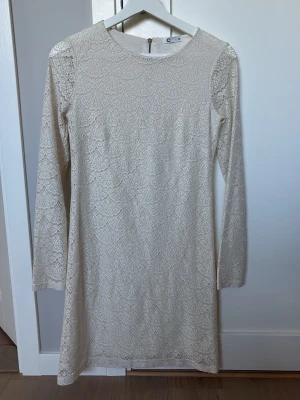 Vit spetsklänning med lång ärm - Säljer en vit kortklänning med vackert spetsmönster och långärmad design. Klänningen har rund halsringning och en diskret dragkedja i ryggen. Perfekt för dig som gillar romantiska detaljer och stilren look.