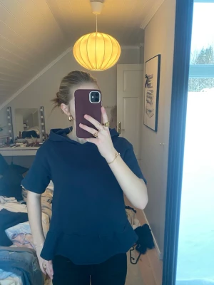 Svart topp med volang och huva - Säljer en svart topp med korta ärmar, volang nertill och huva. Aldrig använd🥰