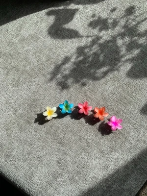 Fem söta hårklämmor 🌺🌺🌺🌺🌺 - Säljer fem färgglada hårklämmor i form av blommor i färgerna gul, blå, rosa, orange och ljusrosa. Klämmorna är gjorda i plast och har en glansig finish. Perfekta för att piffa upp frisyren med en lekfull och färgstark detalj.