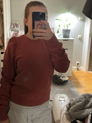 Rostbrun sweatshirt med puffärm - Säljer en rostbrun sweatshirt med rund hals och puffade axlar. Tröjan har långa ärmar och breda muddar vid ärmslut och nederkant. Materialet ser ut att vara mjukt och bekvämt, perfekt för en avslappnad look.