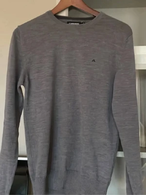 J.Lindberg tröja  - Säljer en stilren grå tröja från J.Lindeberg i storlek S. Tröjan är i bra skick och har en liten logga på bröstet. Perfekt för både vardag och lite finare tillfällen. Den är långärmad och har ribbade muddar vid ärmslut och nederkant. Passar perfekt till vinter. Köpt för 1600 säljer för 600