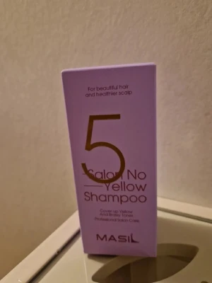 Masil 5 Salon No Yellow Shampoo - Lila förpackning med Masil 5 Salon No Yellow Shampoo, ett professionellt silverschampo som neutraliserar gula toner i blont hår. Perfekt för dig som vill ha kallare nyanser och fräscht hår. Kommer i en stilren kartong med tydlig text.