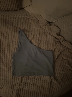 Ljusblå oneshoulder ribbad topp - Trendig ljusblå oneshoulder topp i ribbat material. Perfekt för dig som vill ha en unik och stilren look. Toppen är croppad och har en smickrande passform som passar till både jeans och kjol.