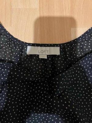 Svart prickig topp från LOFT - Snygg svart ärmlös topp från LOFT med vita små prickar och rundad halsringning. Tillverkad i ett lätt och luftigt material som ger en skön känsla. Perfekt att matcha med jeans eller kjol för en trendig look.