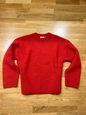 Röd stickad tröja från Weekday - Snygg röd stickad tröja från Weekday med rund halsringning och ribbade muddar. Tröjan har en rak passform och är gjord i ett mjukt, värmande material som passar perfekt till kyligare dagar. Passar S-M