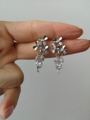 Blommiga silvriga örhängen med pärlor - Unika örhängen i silverfärg med blommiga detaljer och hängande klara pärlor. Blommorna har en modern, stilren design och pärlorna ger extra glans. Perfekta för dig som vill ha något som sticker ut och känns trendigt.