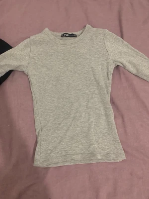 Ljusgrå långärmad topp från Fila - Ljusgrå långärmad topp  i mjukt och stretchigt material. Enkel och slim fit design med rund halsringning, perfekt för att matcha med jeans eller kjol. Diskret logotyp i nacken. Snygg och stilren basic som funkar till många outfits.